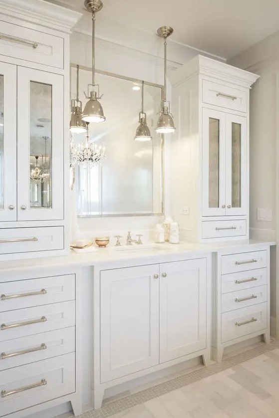 an elegant and stylish creamy bathroom made with vintage kitchen cabinets, a mirror in a metallic frame and vintage pendant lamps