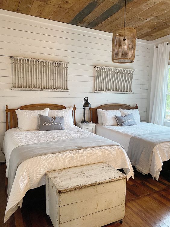 a neutral farmhouse guest bedroom with stained beds, neutral bedding, white shabby chic ladders and whitewashed chests on casters
