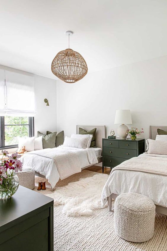 a neutral farmhouse shared guest bedroom with matching beds, neutral bedding, layered rugs, a black dresser, a woven pendant lamp