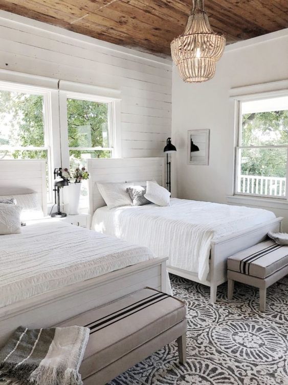 a neutral shared bedroom with a planked accent wall, white planked matching beds, neutral bedding, striped benches and a bead chandelier