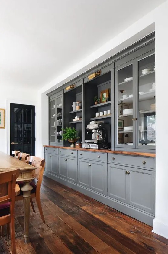 a formal farmhouse dining room with a whole wall taken by grey kitchen cabinets, a vintage wooden dining set