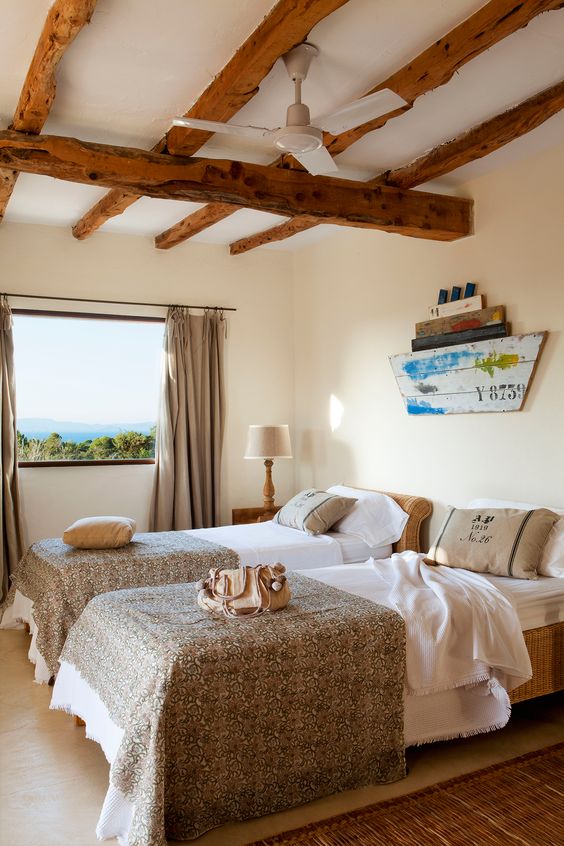a shared coastal bedroom with wooden beams, matching beds, neutral bedding, a ship decoration on the wall