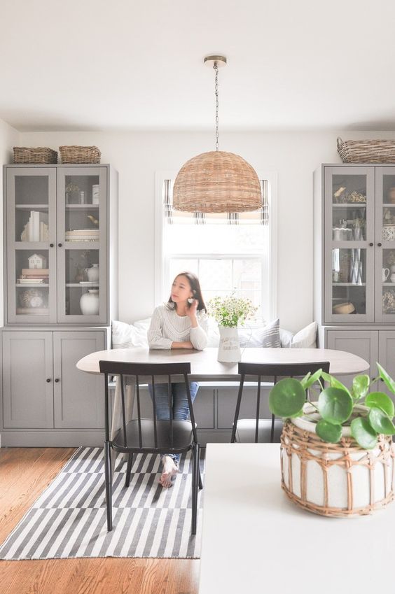 a welcoming farmhouse dining room done with grey kitchen cabinets, an oval table and black chairs, a lovely pendant lamp