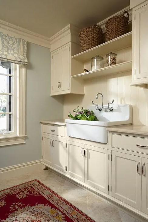 a buttercream laundry with shaker kitchen cabinets, printed textiles, a large sink and baskets for storage