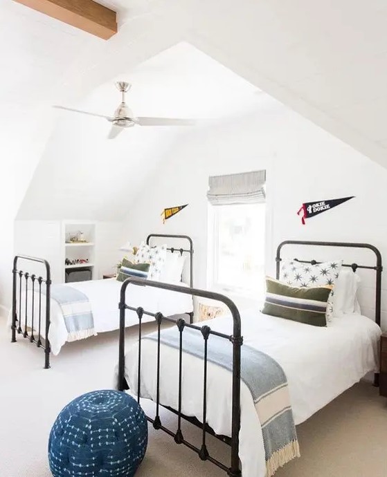 a stylish attic guest bedroom with two beds, a single window with shades and blue touches
