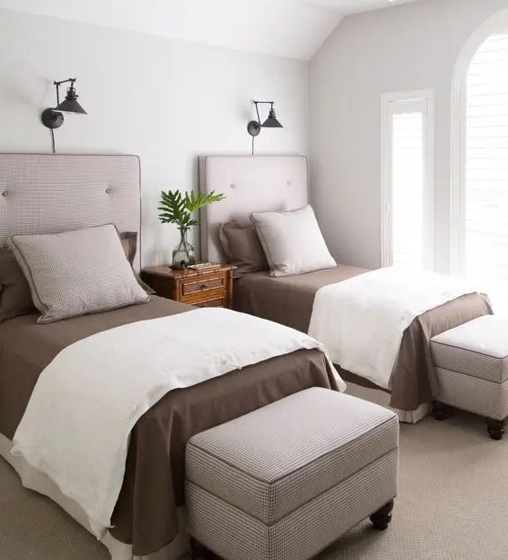a stylish modern guest bedroom with two beds, storage ottomans and some wall lamps is welcoming and cool
