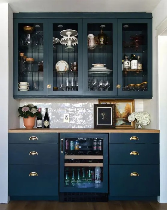 an elegant home bar done with navy kitchen cabinets, glass and usual ones, with a wine cooler and a subway tile backsplash plus a butcherblock countertop