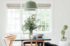 a Nordic dining space with a black dining table, stained chairs and a black bench, green pendant lamps and greneery in a vase