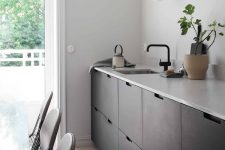 a Scandinavian kitchen with black sleek no hardware cabinetry, a neutral stone countertop and black fixtures is airy and cool
