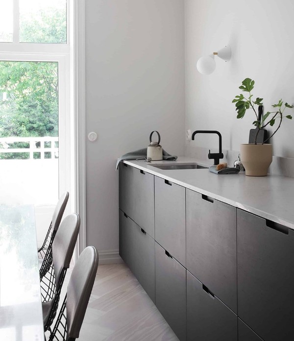 a Scandinavian kitchen with black sleek no hardware cabinetry, a neutral stone countertop and black fixtures is airy and cool