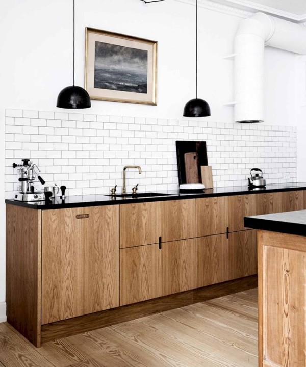 a Scandinavian kitchen with sleek stained cabinets, black stone countertops, a white subway tile backsplash, black pendant lamps