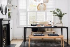 a beautiful Scandinavian dining room with tier on tier shutters, built-in shelves and a cabinet, a non-working fireplace, a black table and benches