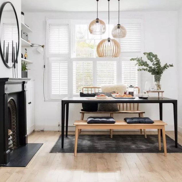 a beautiful Scandinavian dining room with tier on tier shutters, built in shelves and a cabinet, a non working fireplace, a black table and benches
