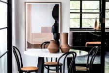 a beautiful and chic dining space by the window, with a round table, black chairs and a statement artwork