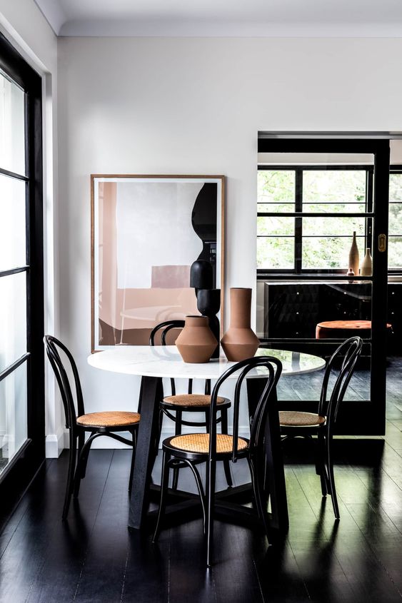 a beautiful and chic dining space by the window, with a round table, black chairs and a statement artwork