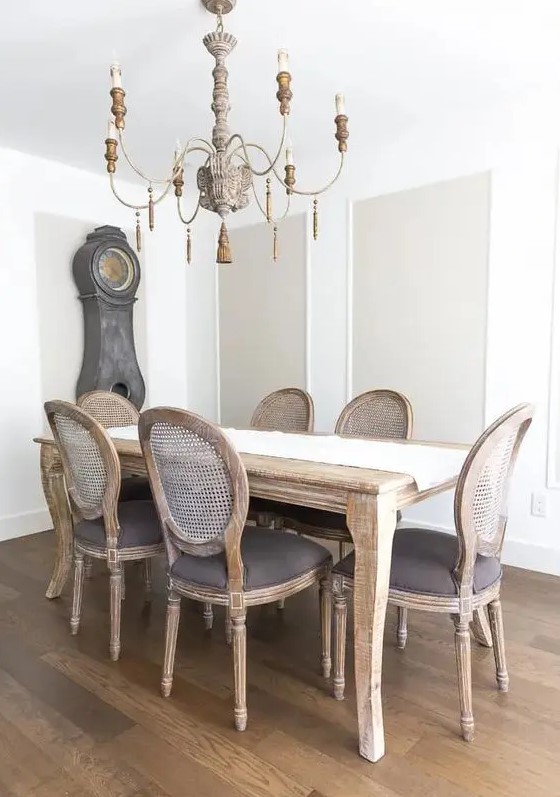 a beautiful and refined French farmhouse dining room with greige touches, a wooden table, reclaimed wood chairs, a vintage chandelier and a clock