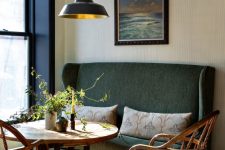 a beautiful and refined dining space with a dark green sofa, a round table and wooden chairs, a retro pendant lamp