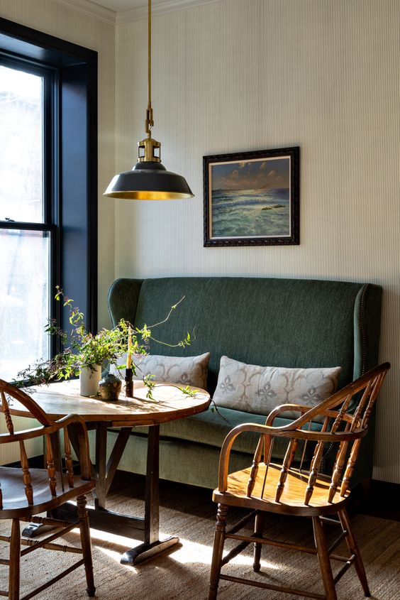a beautiful and refined dining space with a dark green sofa, a round table and wooden chairs, a retro pendant lamp