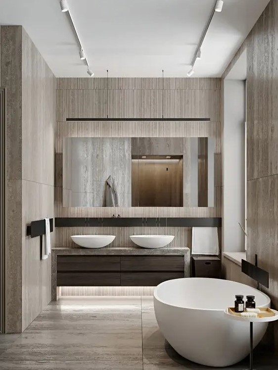 a beautiful bathroom clad with wood imitating tiles, an oval tub and matching sinks, a large mirror and built in lights