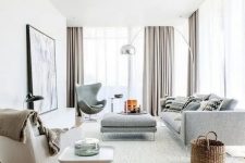 a beautiful contemporary living room with grey and creamy seating furniture, printed pillows, a side table, grey curtains and a basket