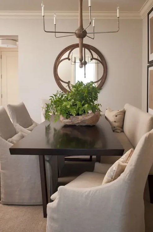 a beautiful neutral vintage dining room with grey walls, a long dark stained table, neutral upholstered chairs, a round mirror and a wooden chandelier