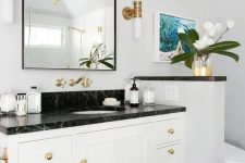 a black and white bathroom with a white vanity with a black countertop and a half wall that separates the toilet from the rest of the space