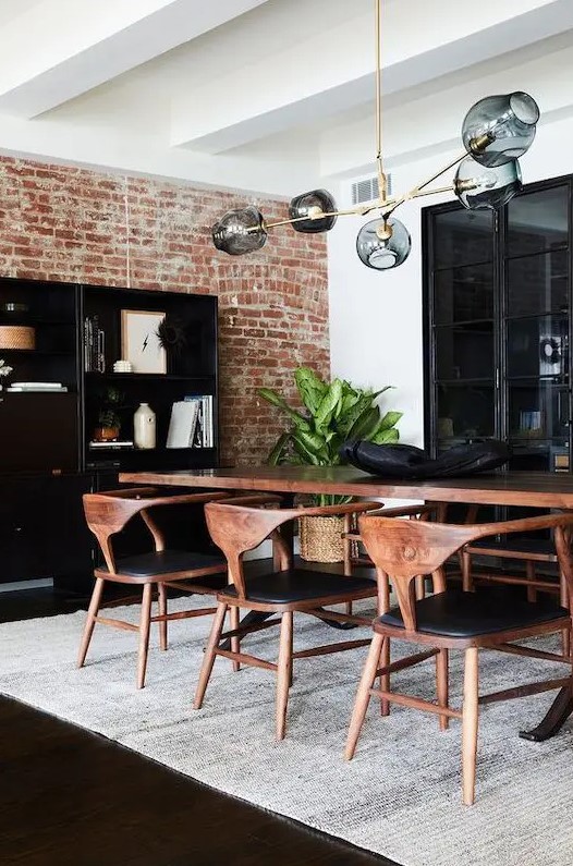 a bold and chic mid century modern dining room with a black storage unit, a stained table and black chairs, a cathy chandelier and potted plants