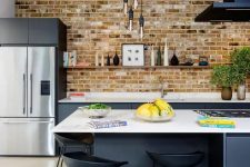 a bold modern kitchen with graphite grey lower cabinets, a brick wall, a black hood, a large kitchen island and black stools