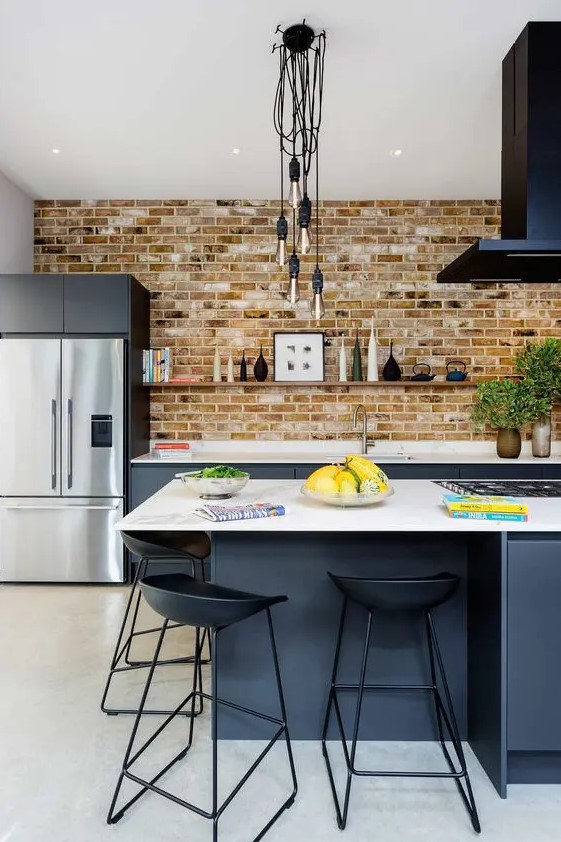 a bold modern kitchen with graphite grey lower cabinets, a brick wall, a black hood, a large kitchen island and black stools