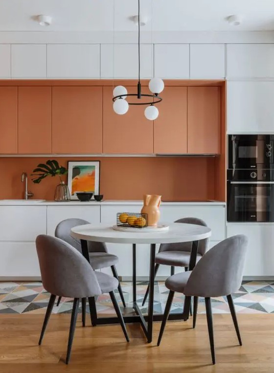a bright contemporary kitchen with orange and white sleek cabinets, an orange backsplash and white countertops, a geo tile floor