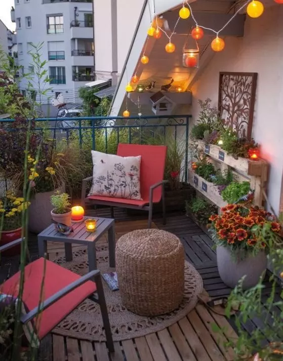 a bright eclectic terrace with a couple of chairs and side tables, a rug, lights and potted blooms and greenery