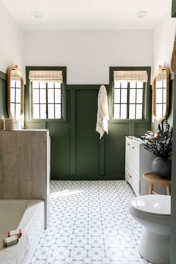 a catchy farmhouse bathroom with green paneling on the walls, a bathtub and a half wall that hides the second vanity