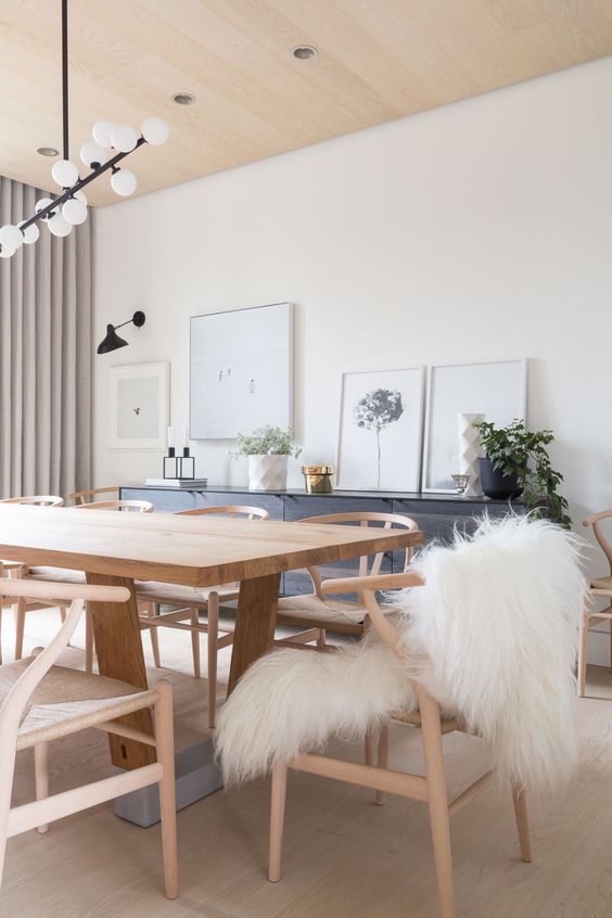 a chic Scandinavian dining room with a grey storage unit, a stained table and chairs, a mid-century modern chandelier and some artworks