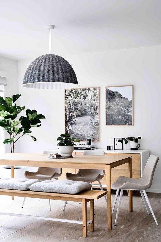 a chic Scandinavian dining space with wooden benches and a matching table, grey chairs, a black pendant lamp and a mini gallery wall