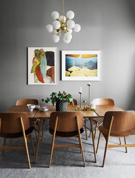 a chic mid-century modern dining room with a stained table and chairs, bright artwork, a chic chandelier and candles in gold candleholders