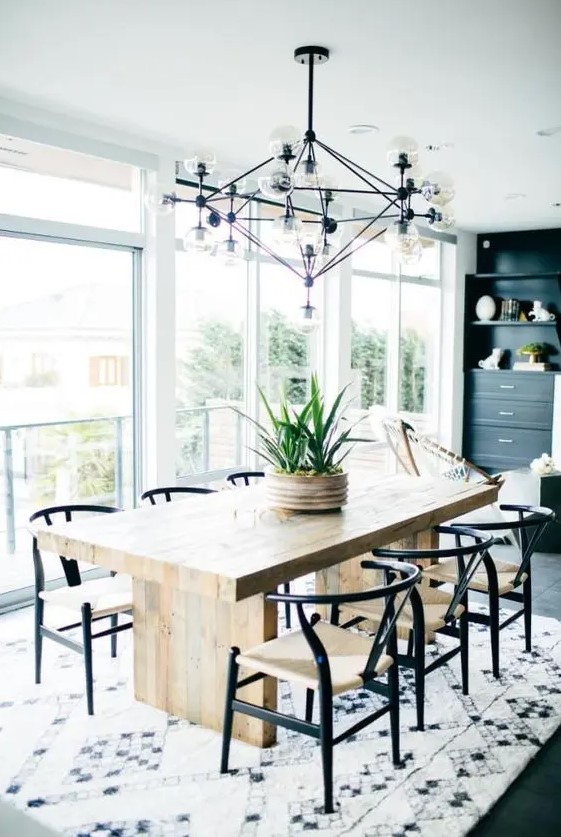 a chic mid-century modern dining space with a stained table and black and white chairs, a printed rug, a black storage unit and a large and cool chandelier