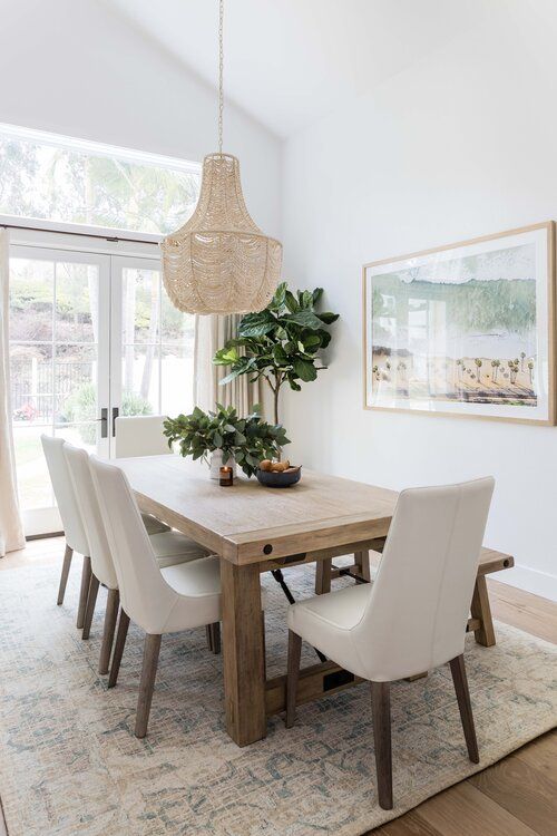 a chic neutral coastal dining space with a stained table, creamy chairs, an artwork and a lovely woven chandelier