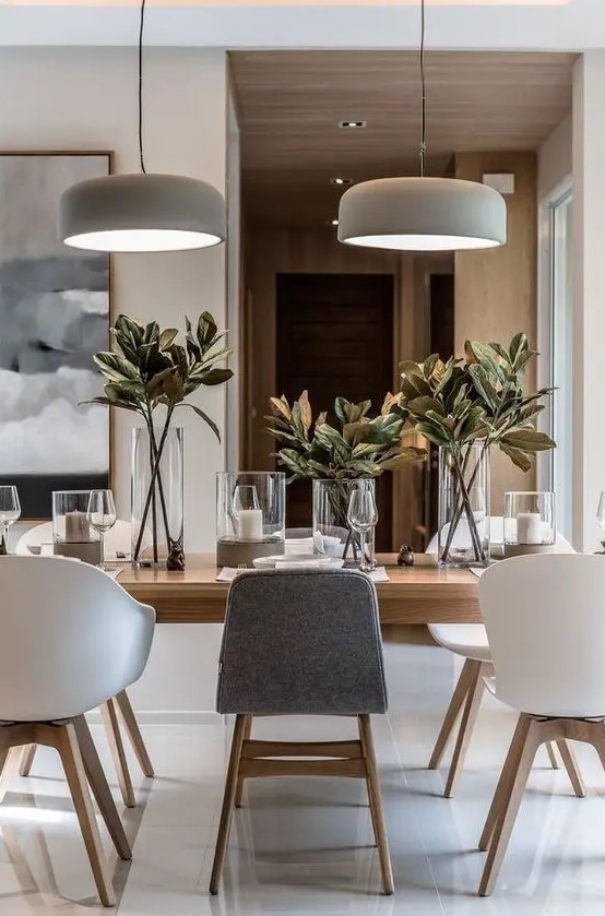 a chic neutral contemporary dining room with a light stained table, white and grey chairs, pendant lamps, candles and foliage