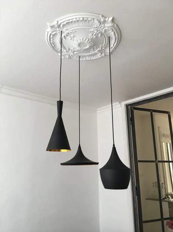 a chic vintage white ceiling medallion with patterns feturing a cluster of modern black and gold pendant lamps looks unusual in contrast with them