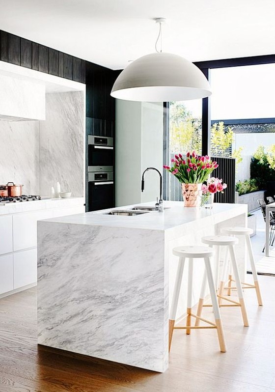 a chic white kitchen with white stone countertops and a backsplash and a waterfall coutnertop on the kitchen island