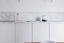 a clean minimalist white kitchen with no hardware cabinets, a white marble tile backsplash and countertops, elegant gold pendant lamps