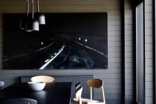 a contemporary and chic dining room with planked walls, a statement artwork, a black table, neutral and black chairs, a cluster of pendant lamps