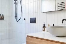 a contemporary bathroom clad with skinny tiles, with a floating vanity, a shower space, a mirror and black fixtures for a contrast