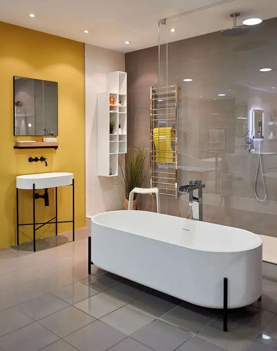 a contemporary bathroom with a grey wall and a yellow one, white appliances, a shower space and a couple of racks for storage