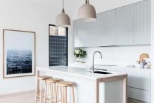 a contemporary beach kitchen with light blue ribbed cabinets and a white kitchen island, wooden stools and pretty pendant lamps
