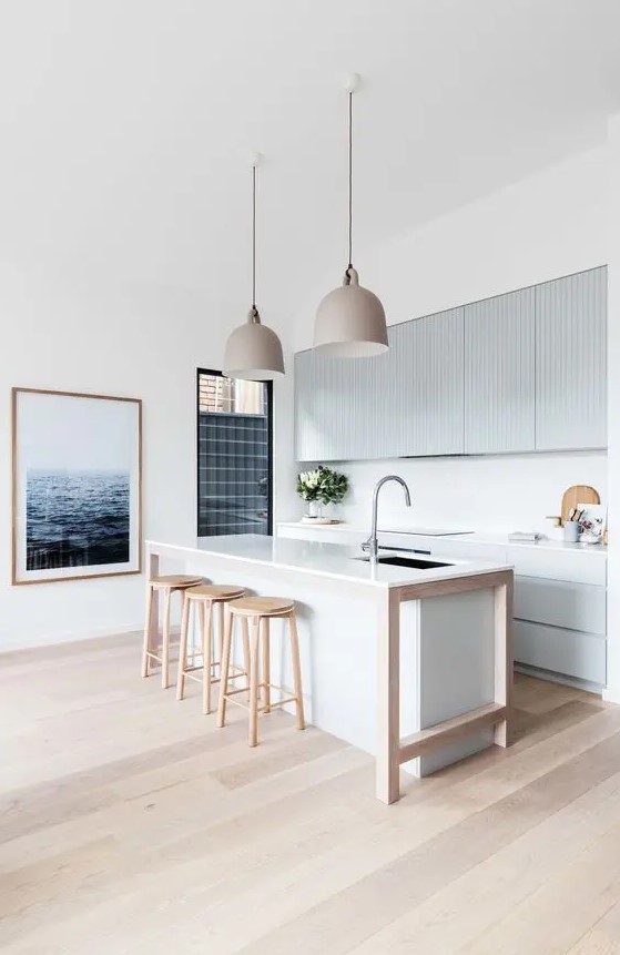 a contemporary beach kitchen with light blue ribbed cabinets and a white kitchen island, wooden stools and pretty pendant lamps