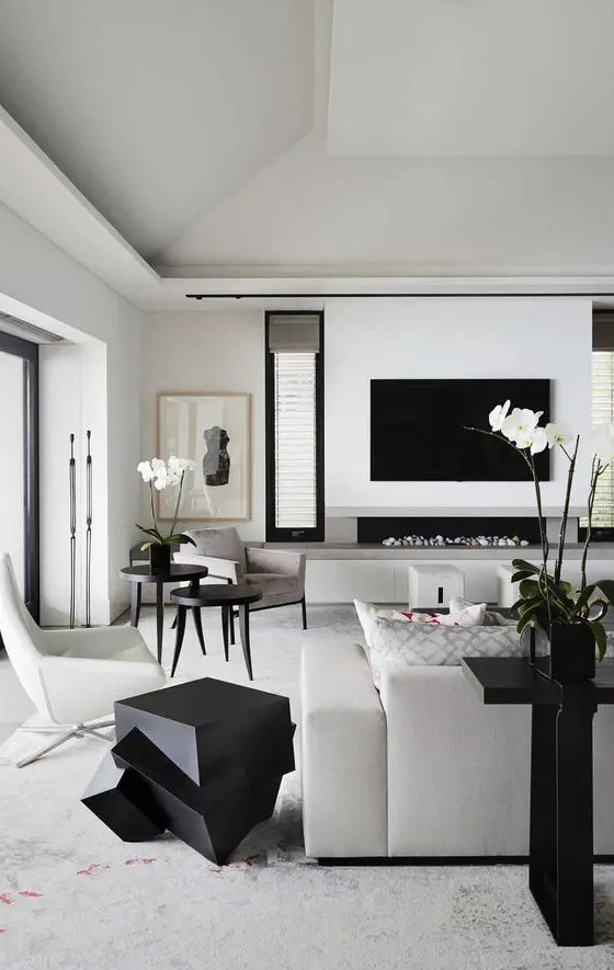 a contemporary black and white living room with a TV, a built in fireplace, creamy and grey furniture, sculptural black tables and a console