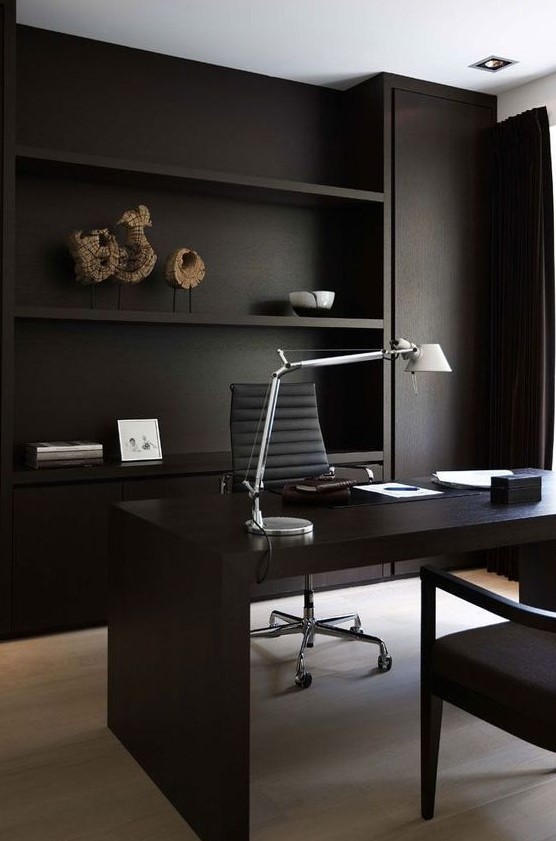 a contemporary black home office with built-in shelves and closed storage, a sleek desk and comfortable chair