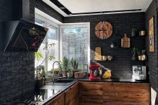 a contemporary black kitchen with black brick walls, light-colored wood cabinets, black countertops and a hood