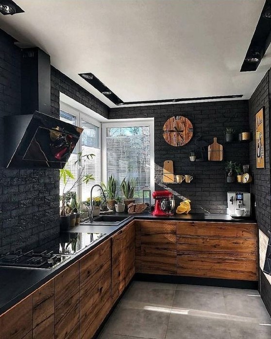 a contemporary black kitchen with black brick walls, light colored wood cabinets, black countertops and a hood
